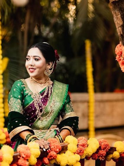 A Maharashtrian bride in a traditional green nauvari saree, posing amidst vibrant marigold decorations. The warm tones and festive setting create a rich and colorful portrait.