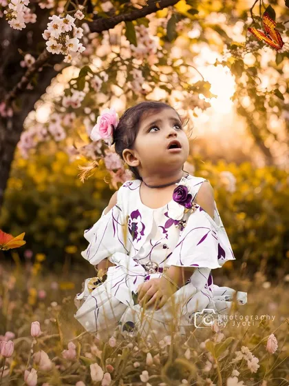 A magical, fairy-tale-like portrait of a little girl in a field of flowers, looking up in wonder at fluttering butterflies that have been artfully edited into the scene.
