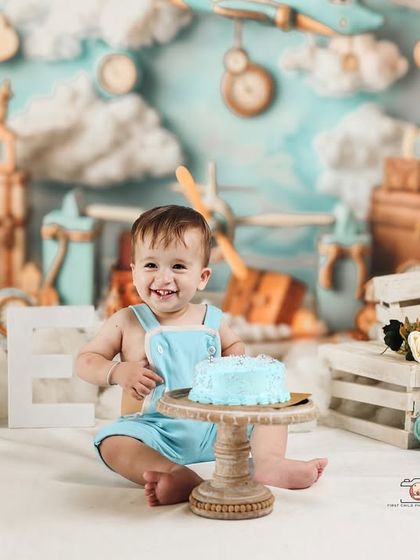 The birthday boy looking absolutely thrilled with his light blue birthday cake. The aviator theme provides a fun and imaginative setting for his first birthday photos.