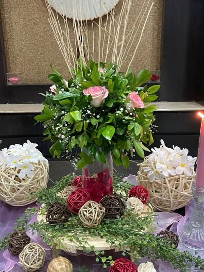 Welcome your guests with flowery vibes. This centerpiece combines a lush bouquet of pink roses and greenery with rustic twine balls and glowing pink candles, creating a warm and inviting atmosphere.