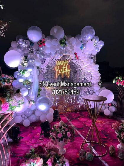 A glamorous rooftop party decoration. This setup features a silver sequin backdrop, a white balloon arch with integrated lights, and a neon sign, creating a stunning look against the night sky.