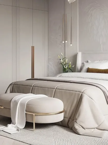 A luxurious bedroom in soft beige tones. The long, elegant handles on the wardrobe and the gold-accented ottoman add a touch of glamour.