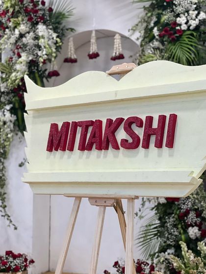 The custom "Mitakshi" name board, with glittering red letters, was a central piece of the naming ceremony decor. It stood proudly, surrounded by red and white flowers that complemented the theme.