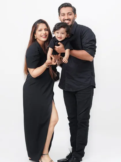A joyful family portrait in matching black attire, with the father lifting their smiling baby boy in the air.