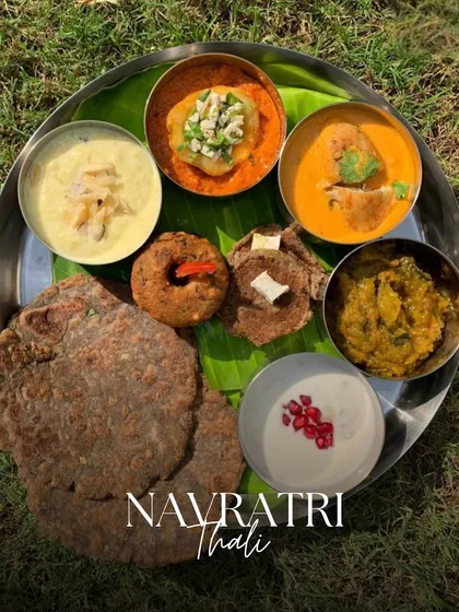 A beautiful Navratri Thali photographed outdoors, featuring a complete meal with kuttu ki puri, sabzis, and raita, all served on a traditional banana leaf.
