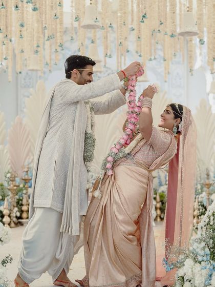 A playful moment during the jaimala exchange. The backdrop features our custom feather-inspired panels and a ceiling of hanging floral strings, creating a textured, multi-layered look.