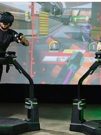 Players aim their controllers in a fast-paced shooting game. The Virtuix Omni allows for natural movement, including strafing and turning, providing an unparalleled level of immersion for competitive action.