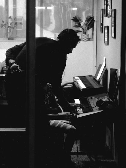 A teacher provides individual guidance during a piano lesson. This black and white shot captures a quiet moment of focused learning.