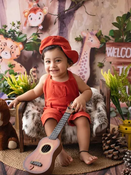 Before the cake smash. A happy one-year-old boy in a jungle-themed setup, holding a ukulele.