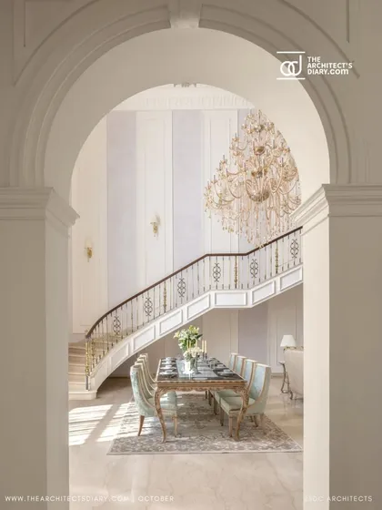 A view through a stately archway frames the grand staircase and formal dining area of The Ivory Royale. This composition highlights the home's layered design, where each space is elegantly revealed from the next.