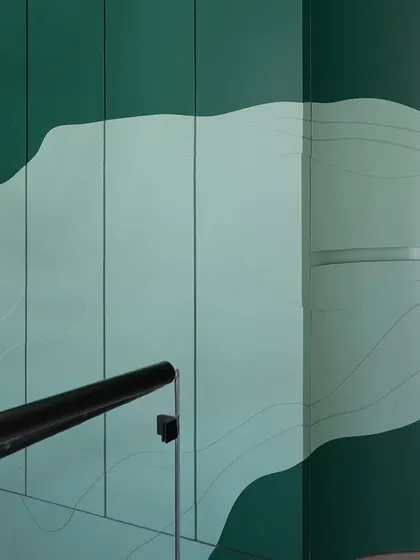 A close-up of the custom green paneling in the staircase well. The layered, topographic-like design conceals a secondary access door, seamlessly blending functionality with artistic expression.