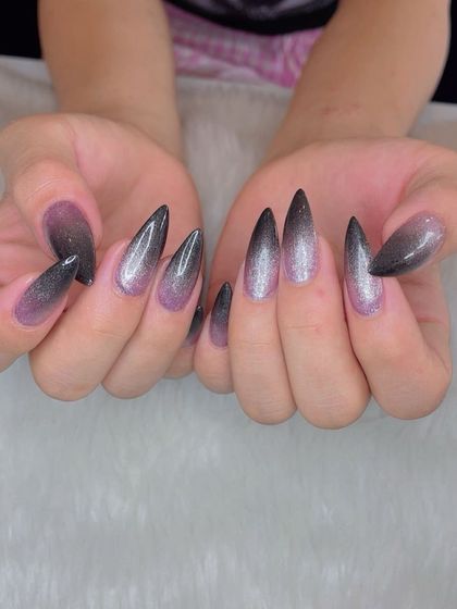 A dramatic ombré glitter effect on sharp stiletto nails. The color fades from a soft pink at the base to a deep, glittery black at the tips for a truly magical look.