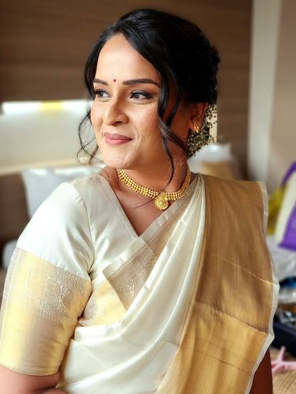 A radiant portrait of the bride in her Kasavu saree. The makeup is clean and sculpted, with a focus on her beautiful features and glowing skin.
