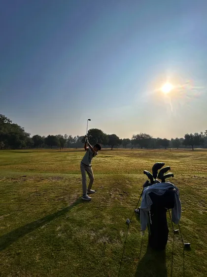 A young golfer takes a full swing under the bright sun, with his golf bag in the foreground.