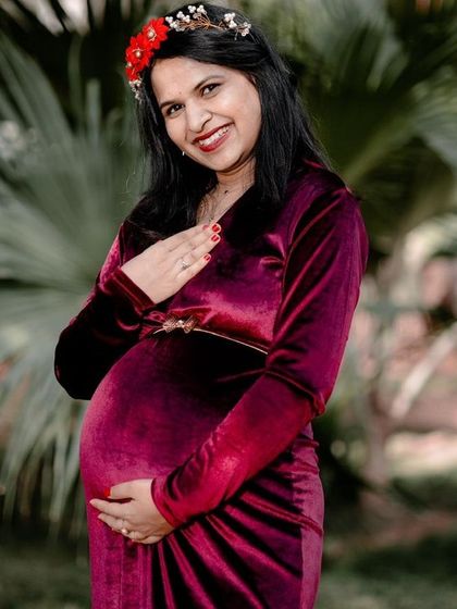 A classic maternity pose, with the mother-to-be cradling her bump. The vibrant color of her dress and floral crown stand out beautifully against the green background.