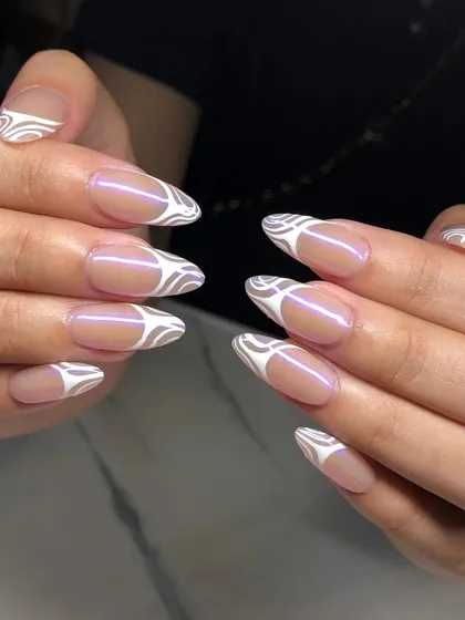 A modern and graphic design with a sheer nude base and a swirling white pattern on the tips of these almond nails.