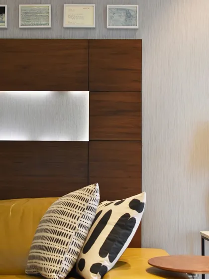 The same yellow sofa is seen here with a wood-paneled headboard feature, showcasing its versatility against different textures and patterns.