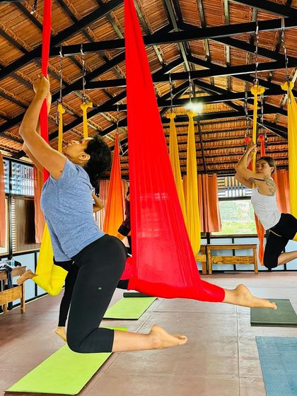 A student practices a kneeling lunge variation in the red hammock, using the silk to deepen the stretch in her hip flexors.