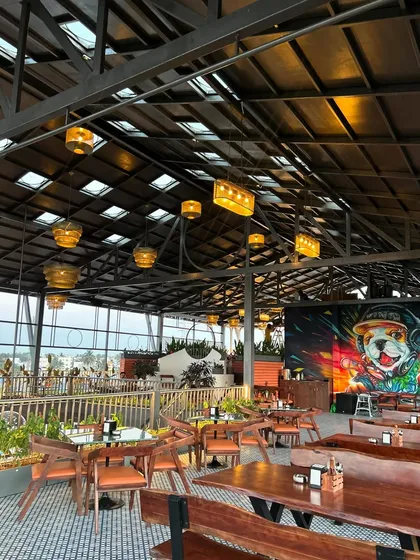 This shot of The Soda Factory showcases the full ambiance at dusk. The strategic placement of plants around the seating areas and the vibrant wall mural come together to create an energetic and inviting atmosphere for guests.