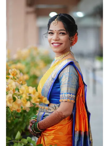 A radiant bride in a vibrant yellow and blue saree. Her happy smile and the colorful flowers beside her create a cheerful and beautiful portrait.
