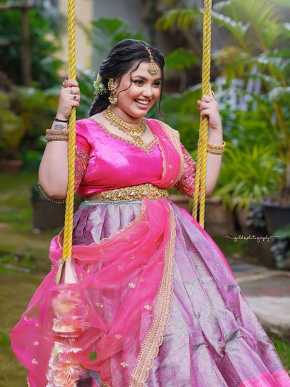 A cheerful and vibrant outdoor shoot featuring a model in a pink and purple half-saree. The playful poses on a swing and the bright colors capture a youthful and joyous spirit.