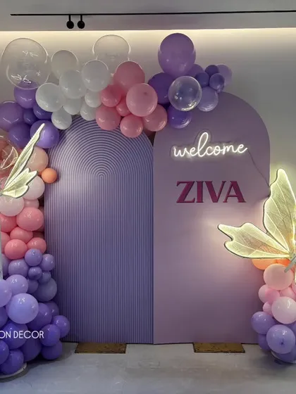A chic and modern welcome decoration for baby Ziva. This setup uses pastel arched backdrops, organic balloon arrangements, and custom neon signage, complemented by elegant light-up butterfly props.
