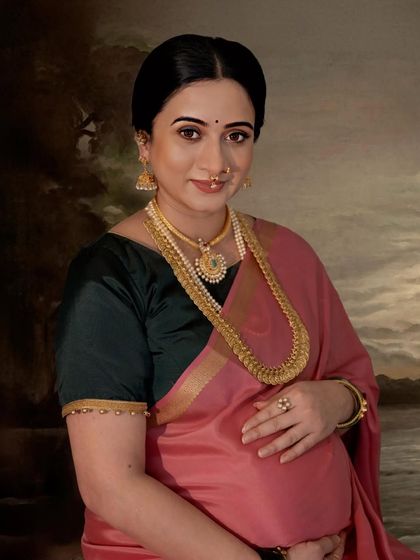 A close-up portrait inspired by Raja Ravi Varma's art. The mother-to-be is adorned with traditional gold jewelry and a pink saree, her expression serene and painterly.