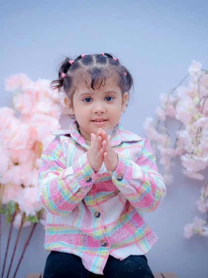 A sweet girl with her hands together, posing in front of a cherry blossom backdrop. We guide children into poses that feel natural and fun.