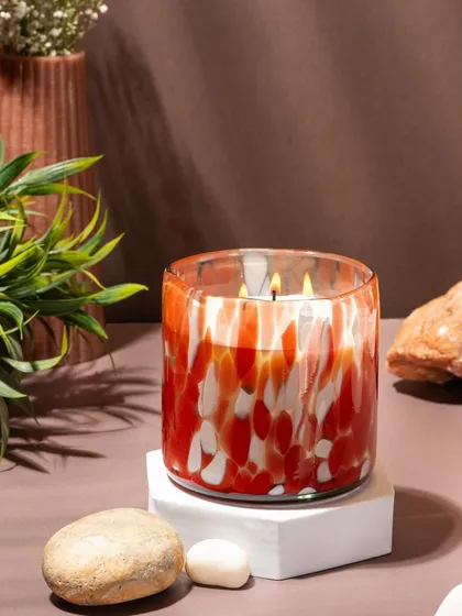 A lifestyle shot of a red and white marbled glass candle from Lighthouse. The warm, earthy tones of the background create a cozy and inviting atmosphere.