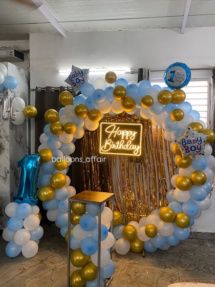 A first birthday party for a baby boy with a blue, white, and gold circular balloon arch.
