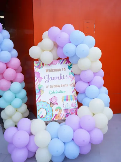 A personalized welcome sign for Jaanki's 3rd birthday party, featuring a sweet donut and candy theme surrounded by pastel balloons.