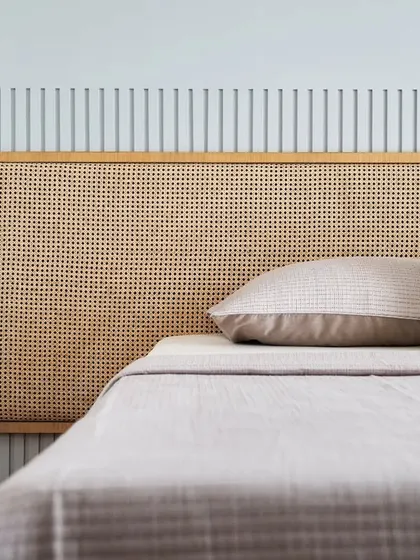 A detailed shot of the custom-designed oak and rattan headboard. The natural weave of the cane adds a delicate, handcrafted texture that is central to the room's calming design.