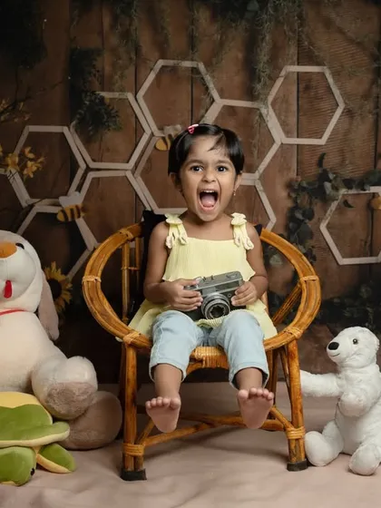 Let your child's imagination run wild in our creative studio sessions. Here, a curious toddler becomes a little photographer, surrounded by her favorite toys in a whimsical, honey-bee themed setup.