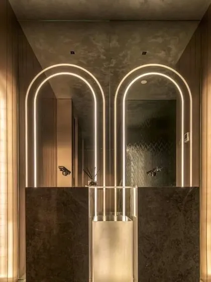 We believe every part of a home deserves great design. This wash area features custom arched backlit mirrors and warm, vertical wall paneling, turning a simple utility space into a statement of modern elegance.