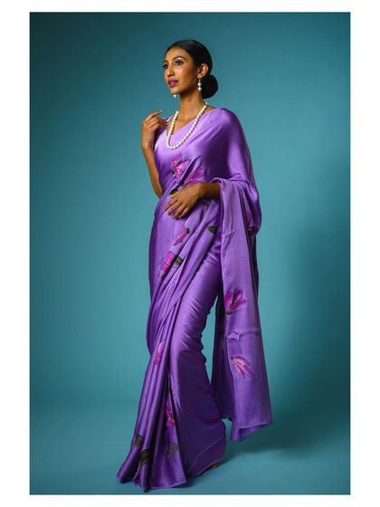 A full-length studio shot of a model in a flowing purple saree against a solid blue background. The clean, professional lighting and elegant pose make this ideal for an e-commerce catalog or brand lookbook.