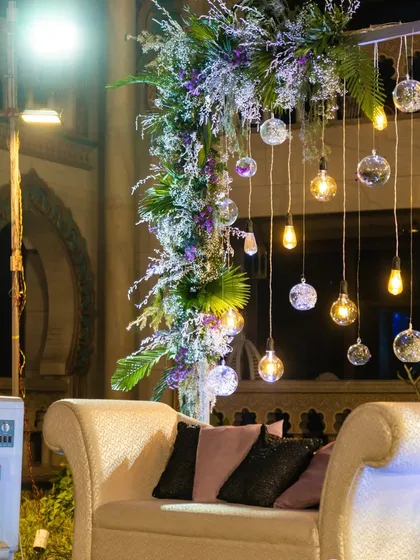 A close-up of the photo booth decor, highlighting the mix of greenery, purple flowers, and the warm glow of the hanging bulbs.