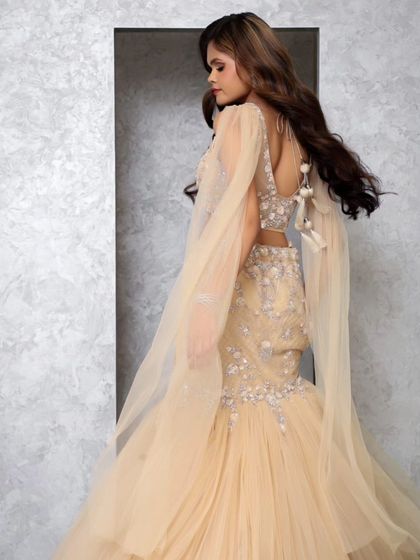 The back view of the beige mermaid gown, highlighting the flowing cape that adds a touch of drama and movement to the outfit.