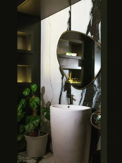 The powder room in this project features a striking black panda marble on the feature wall, paired with a minimalist pedestal sink and a pebble-shaped mirror for a dramatic, artful look.