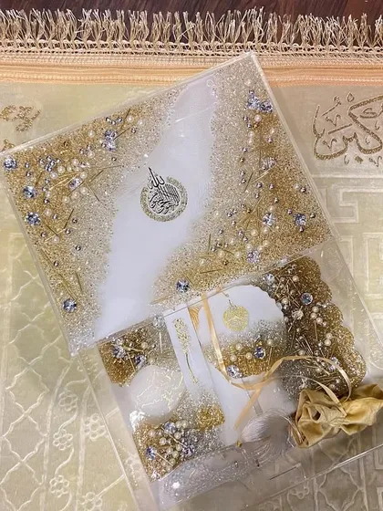 An elegant gift set in white and gold, perfect for Eid or any special occasion. This set includes a resin Quran box, a matching bookmark, and other accessories, all embellished with crystals and pearls for a luxurious finish.