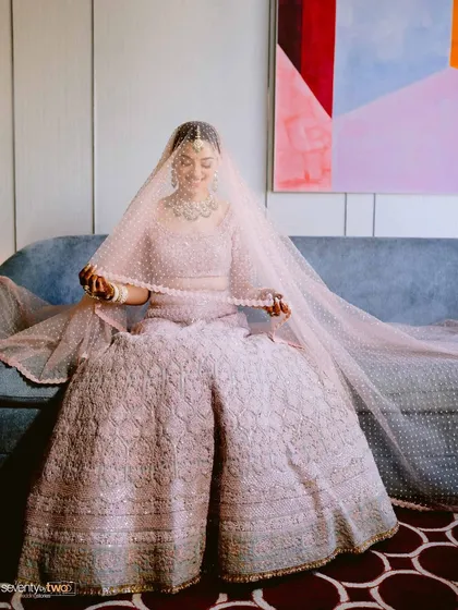 The bride sits on a couch, her face veiled, creating a soft and romantic portrait full of anticipation.