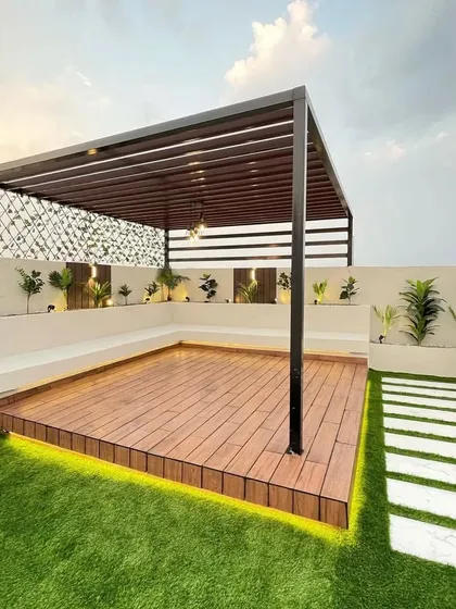 We built this expansive terrace retreat to be both beautiful and practical. The design features a sleek black pergola over a raised wooden deck, surrounded by durable artificial grass that stays green all year. The built-in bench seating provides ample space for guests, while the stone pathway adds a touch of elegance to the outdoor garden design.