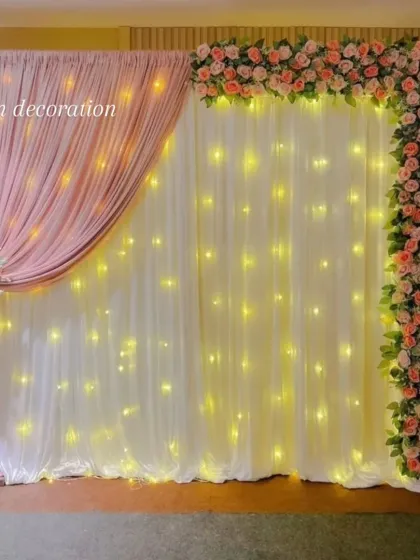 A clear, straight-on shot of the fabric drape backdrop with warm fairy lights and an artificial flower border.