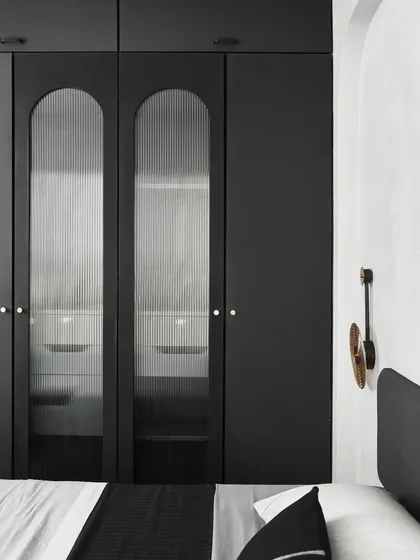 The matte black laminated closet in 'The Pier' bedroom features fluted curved glass, adding texture and sophistication. The design was inspired by the calm after a storm.