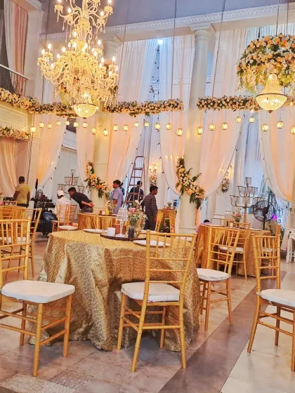 An elegant indoor hall setup for a reception dinner, showing the guest tables with golden tablecloths and the grand chandeliers I installed.