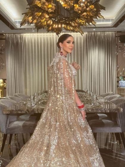 The bride strikes a pose, showing off the incredible detail of her caped lehenga. The sleek bun and smokey eyes add to the regal feel.