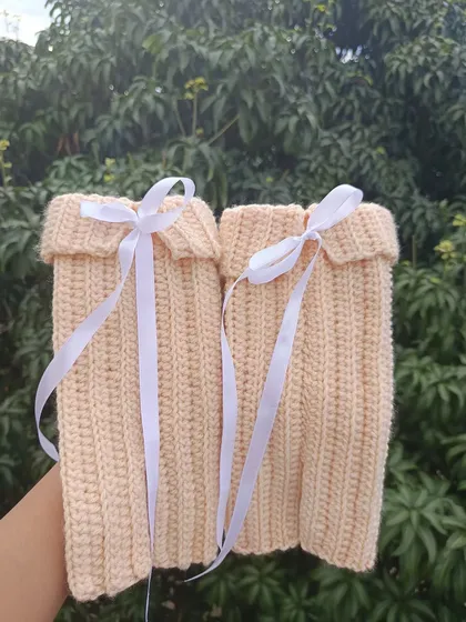 A pair of cozy, custom-made leg warmers in a soft peach color with white ribbon ties. A perfect accessory for colder weather.