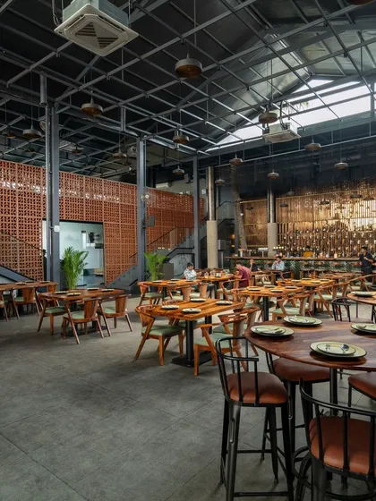 This wide-angle view showcases the scale of the double-volume dining space and two of our signature elements. The rustic terracotta partition wall adds warmth and texture while screening private areas, contrasting beautifully with the industrial metal and concrete surfaces of this modern pub interior.