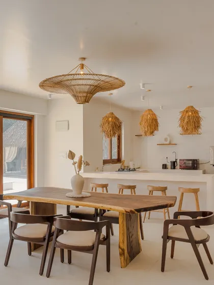 The dining area combines a rustic live-edge wooden table with modern chairs and statement rattan pendant lights, creating a perfect setting for shared meals.