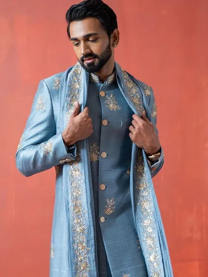 A beautiful light blue sherwani set, complete with an embroidered inner kurta and a matching stole. The gold embroidery provides a subtle contrast, ideal for a sophisticated groom.