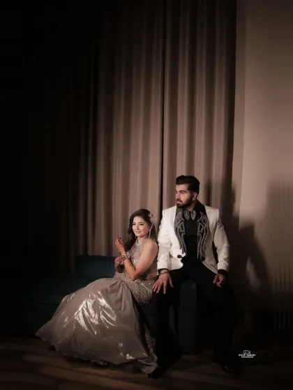 An elegant and moody indoor portrait, using dramatic lighting to highlight the couple's glamorous attire and create an atmosphere of sophisticated romance.